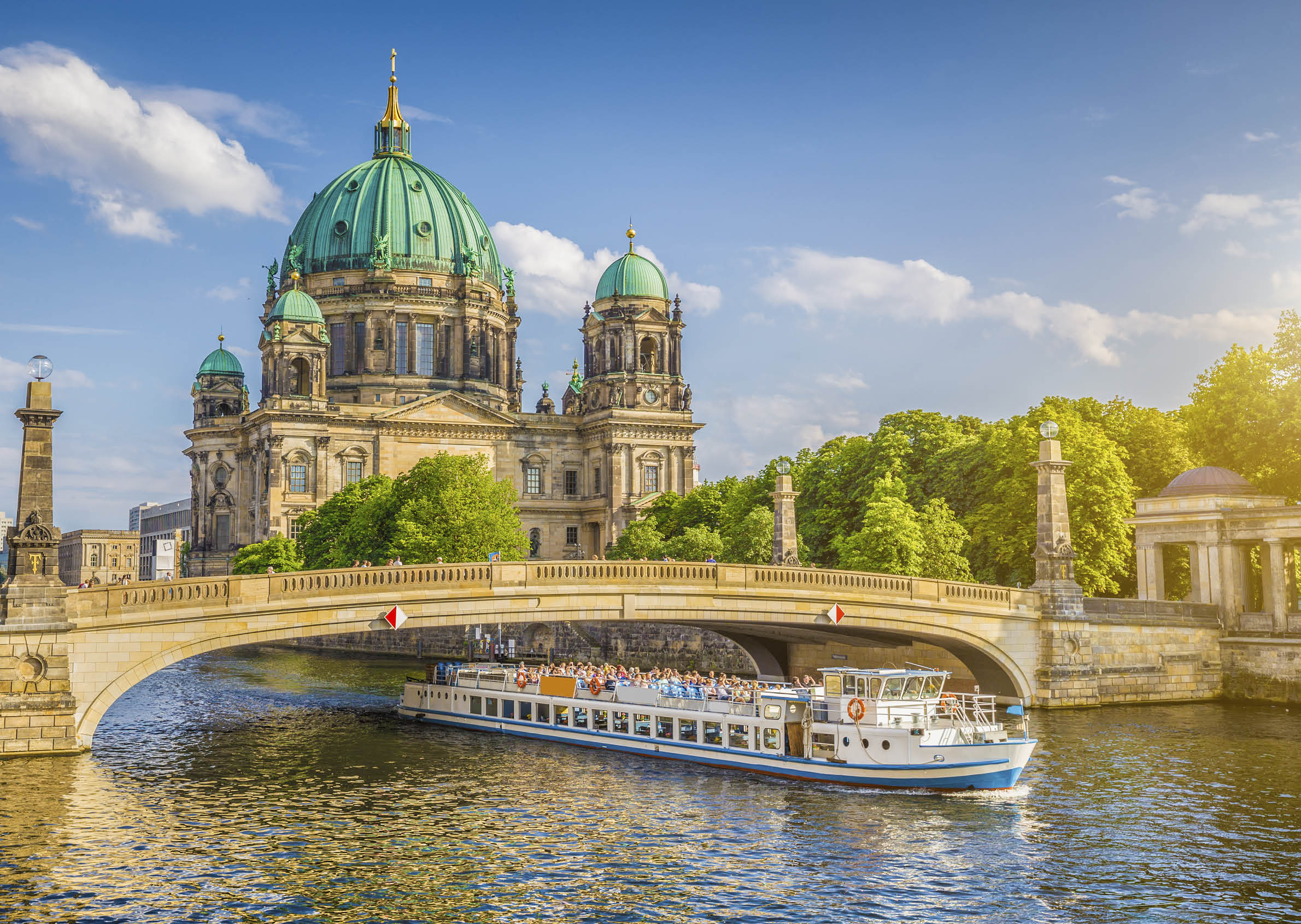 Beautiful view of historic Berlin Cathedral (Berliner Dom) at famous Museum Island with ship passing Friedrichsbrucke bridge on Spree river in golden evening light at sunset in summer, Berlin, Germany