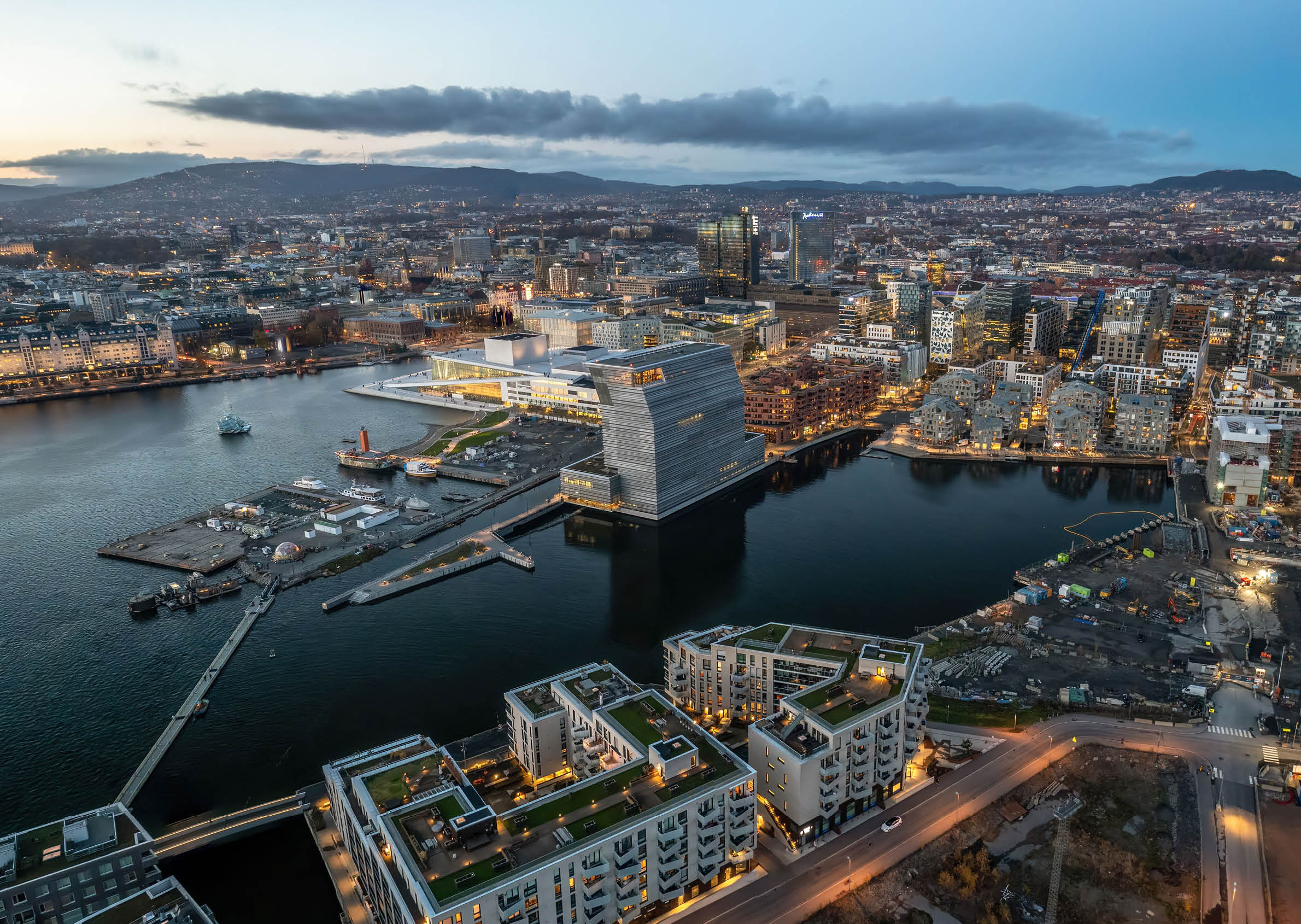 An aerial shot of Oslo at sunset, with lots of buildings and lights, surrounded by sea, Norway