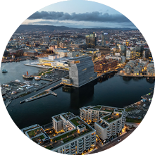 An aerial shot of Oslo at sunset, with lots of buildings and lights, surrounded by sea, Norway