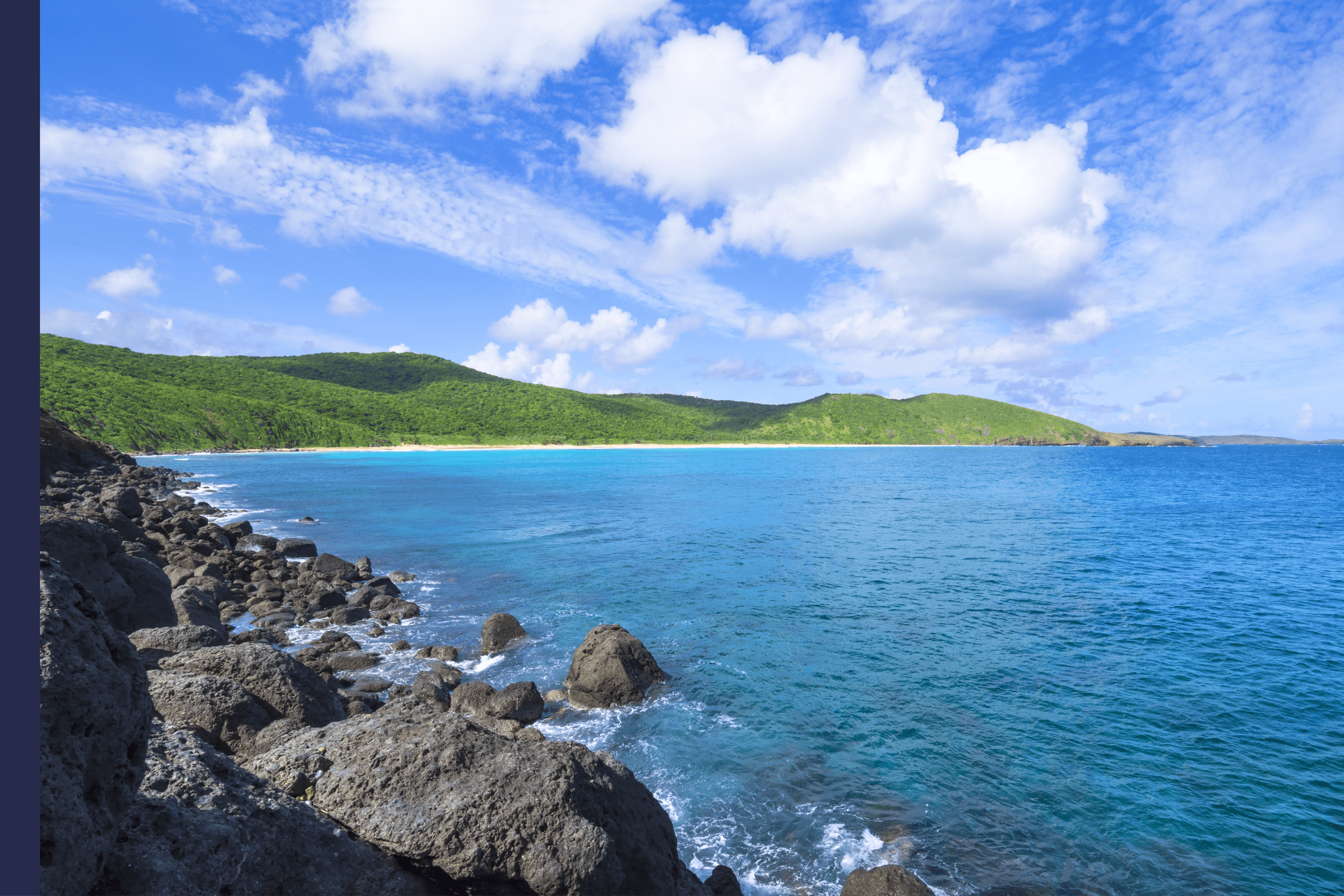 Rugged dark boulders contrast wide sandy beach and rolling green hills of Resaca Beach on the Caribbean island of Isla Culebra in Puerto Rico